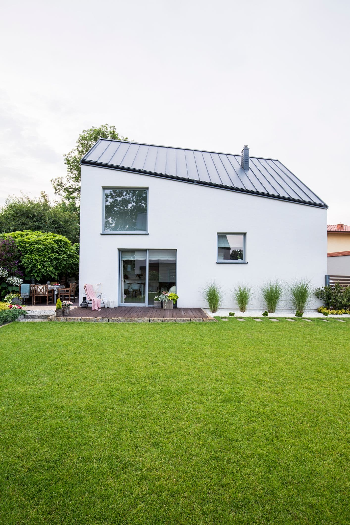Zadní pohled na moderní rodinný dům s terasou a velkými okny, obklopený udržovanou zahradou.